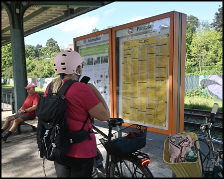 Eine Radfahrerin betrachtet einen orangfarbenen Fahrplanaushang