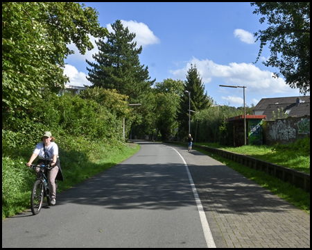 Alte Bahnsteigkanten am Rande eines Bahntrassenradweges mit einer Fahrradfahrerin