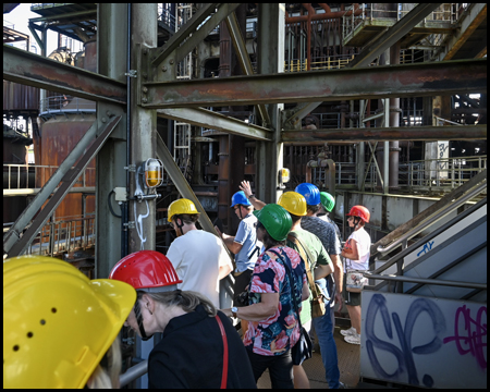 Besucher mit bunten Helmen in einer Industriekulisse