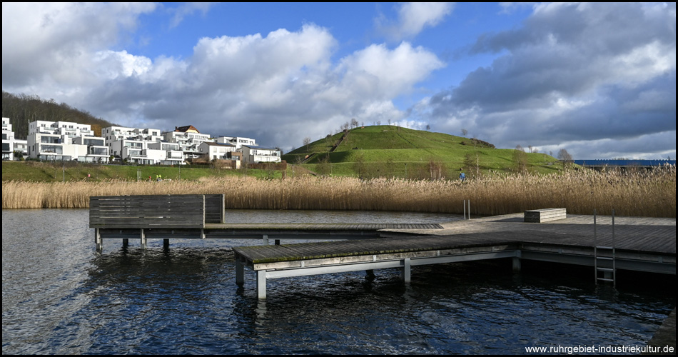 Ein Hügel hinter einem See mit Stegen und Schilf