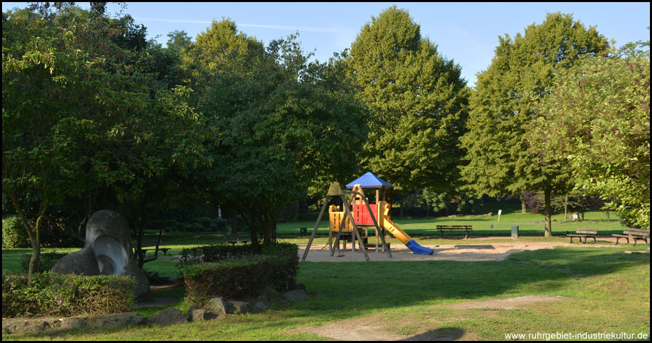 Einer von mehreren Spielplätzen und Aktionspunkten samt Sitzbänken unter Bäumen im Revierpark Mattlerbusch