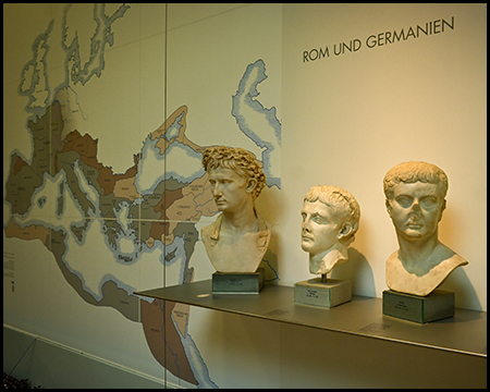 Ausstellungsbereich "Rom und Germanien" mit drei römischen Kaiserbüsten auf einem Regal. Im Hintergrund ist eine große Wandkarte mit dem Römischen Reich und Germanien zu sehen, die die geografischen Zusammenhänge illustriert.