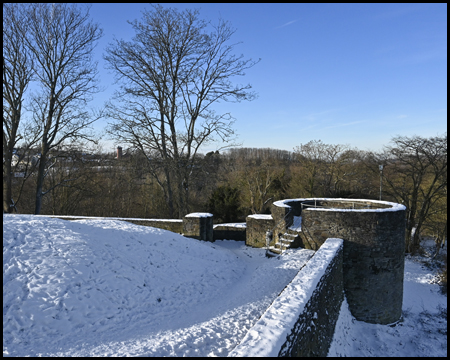 Mauer und Rundturm auf einem Ruinen-Gelände mit Wiese und Bäumen mit Schnee