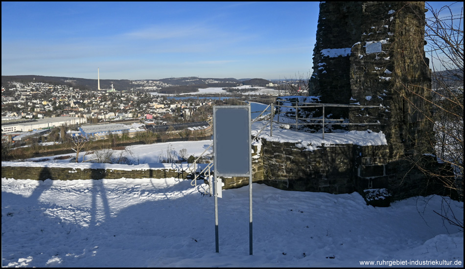 Markanter halber Turm der Ruine Volmarstein und Teil des Geländes mit Infotafel im Schnee. Hinten Aussicht ins Ruhrtal