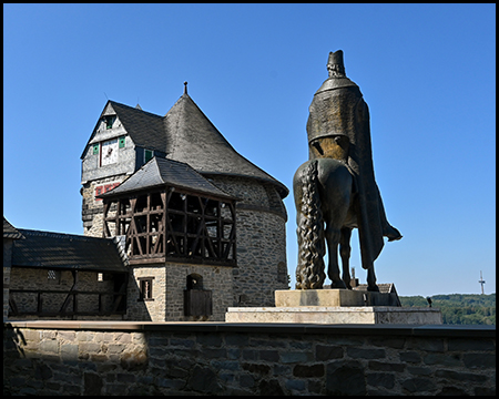 Ein bronzenes Reiterstandbild vor einem Fachwerkturm mit spitzem Dach.