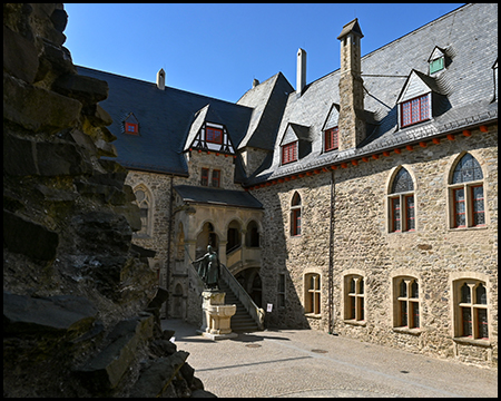 Ein Innenhof der Burg mit Freitreppe und Statue vor Bruchsteinmauern.
