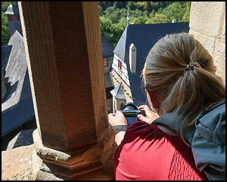 Eine Person fotografiert mit einer Kamera von einem Turm aus, im Hintergrund Dächer und Fachwerkhäuser.