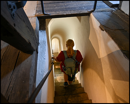 Eine Person geht eine enge, gewölbte Treppe in einem Turm hinunter.
