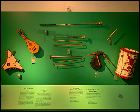 Historische Musikinstrumente wie Trompeten und eine Trommel an einer grünen Ausstellungswand.