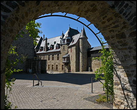 Blick durch einen Torbogen auf die Schlossanlage mit Türmen und Fachwerkelementen.