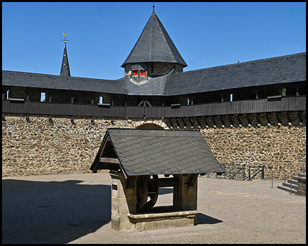 Ein hölzerner Brunnenüberbau auf dem Burghof, im Hintergrund ein Turm