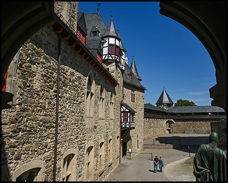 Blick durch einen Torbogen auf einen Burghof mit Fachwerkelementen und einer Statue.