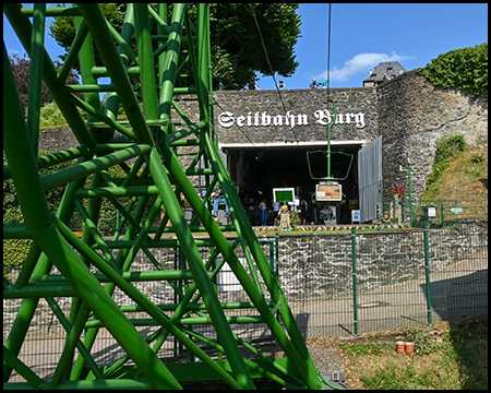 Der Eingang einer Seilbahnstation mit der Aufschrift „Seilbahn Burg" hinter einem grünen Gittermast.