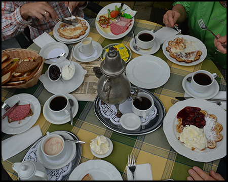 Ein reich gedeckter Kaffeetisch mit Waffeln, Brot, Aufschnitt und mehreren Tassen Kaffee.