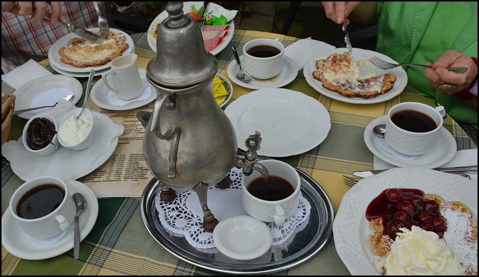 Eine Kaffeekanne auf einem Tablett inmitten eines gedeckten Tisches mit Waffeln und Gebäck.
