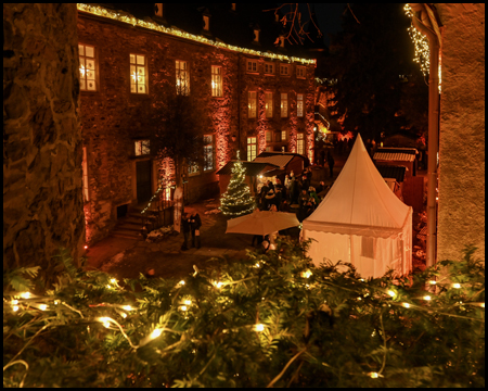 Hof von Schloss Hohenlimburg mit einem Weihnachtsmarkt. Im Vordergrund Lichterkette über einer Hecke
