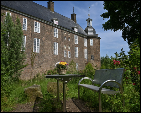 Ein Rastplatz mit Tisch und Bank und Blumen auf dem Tisch vor dem Schloss Ringenberg