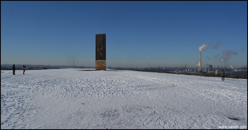 Die 15 Meter hohe "Bramme für das Ruhrgebiet" auf dem Gipfel der Schurenbachhalde. Rechts dampft die Kokerei Prosper
