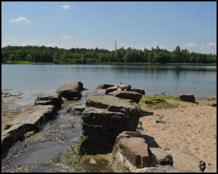 Plätschernder Bachlauf am Badestrand, hinten die Bergehalde