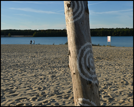 Mit Mustern bemalter Baumstamm an einem Strand