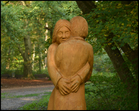 Eine Holzskulptur im Wald mit zwei sich umarmenden Frauen