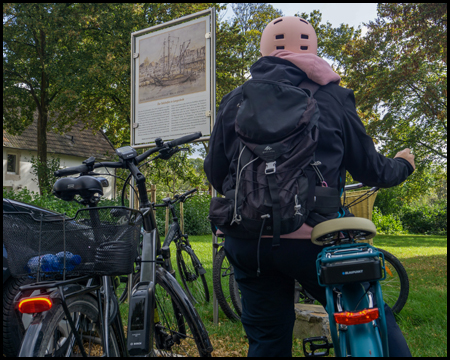 Zwei Fahrräder und eine Radfahrerin vor einer Infotafel zum Salzhafen Langschede