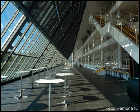 Im Innern vom Wissenschaftspark Rheinelbe mit einem langen Atrium mit Tischen und einer Glasfront auf einer Seite.