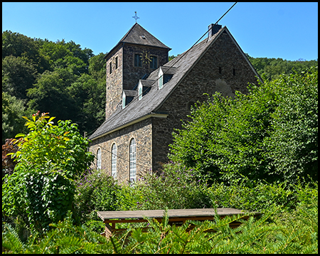 Eine steinerne Kirche mit Turm und Uhr, umgeben von Sträuchern
