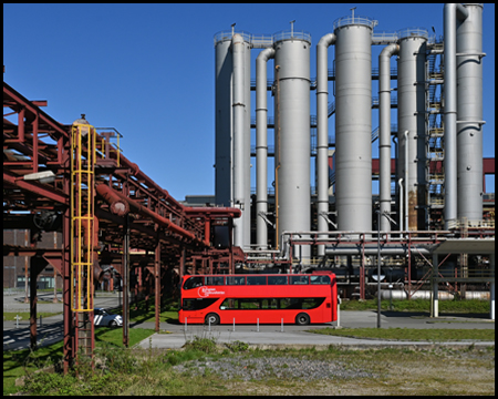 Roter Bus vor einer Industriekulisse von Silos und Rohrleitungen